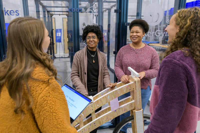 A diverse group of female Mechanical Engineering students gather around a wooden bike built for a competition.