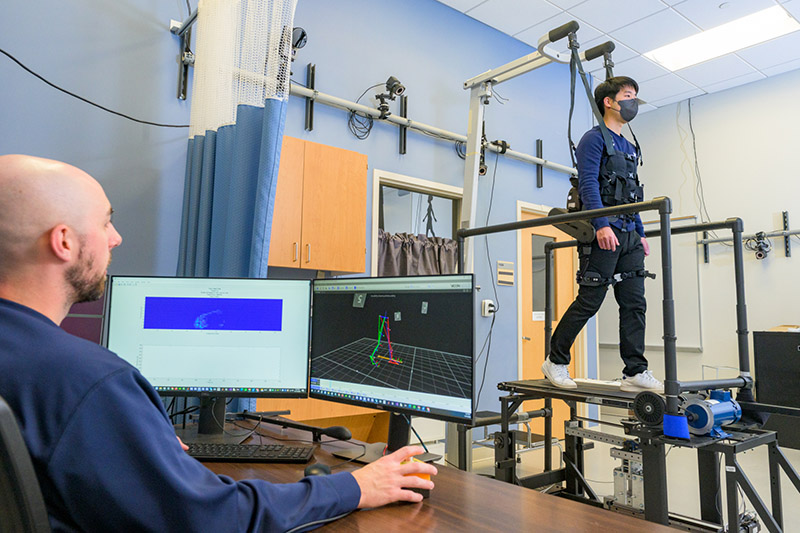 Doctoral student GilHwan Kim (right) demonstrates the robotic device and adaptive treadmill set-up, a unique approach that more closely mimics how patients will respond in real-world settings.
